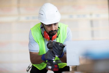 Beyaz miğferi ve güvenlik yeleği olan işçi ahşap bir ev inşa ediyor.