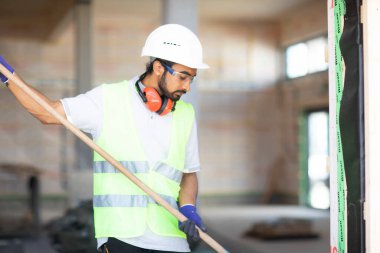 Beyaz miğferi ve güvenlik yeleği olan işçi ahşap bir ev inşa ediyor.