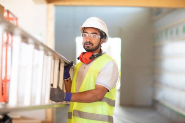 Beyaz miğferi ve güvenlik yeleği olan işçi ahşap bir ev inşa ediyor.