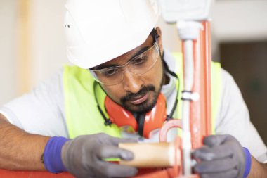 Beyaz miğferi ve güvenlik yeleği olan işçi ahşap bir ev inşa ediyor.