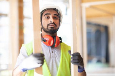 Ahşap bir binada beyaz kasklı ve güvenlik yelekli bir işçi.