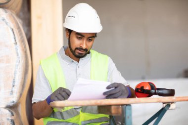 Ahşap bir binada beyaz kasklı ve güvenlik yelekli bir işçi.