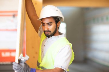 Ahşap bir binada beyaz kasklı ve güvenlik yelekli bir işçi.