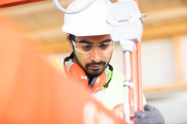 Beyaz miğferi ve güvenlik yeleği olan işçi ahşap bir ev inşa ediyor.