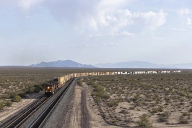 Uzak konteyner yığını treni çöl ortamına yaklaşıyor.