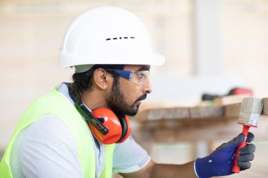 Beyaz miğferi ve güvenlik yeleği olan işçi ahşap bir ev inşa ediyor.