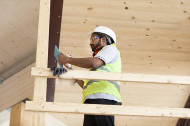 Ahşap bir binada beyaz kasklı ve güvenlik yelekli bir işçi.