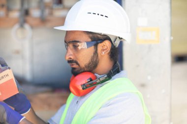 Beyaz miğferi ve güvenlik yeleği olan işçi ahşap bir ev inşa ediyor.