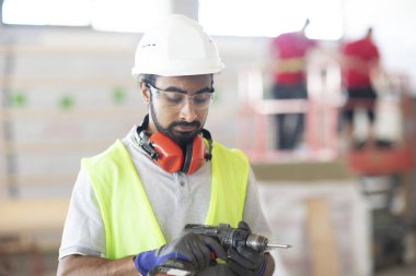 Beyaz miğferi ve güvenlik yeleği olan işçi ahşap bir ev inşa ediyor.