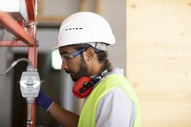 Beyaz miğferi ve güvenlik yeleği olan işçi ahşap bir ev inşa ediyor.