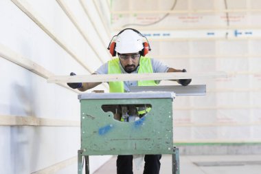 Ahşap bir binada beyaz kasklı ve güvenlik yelekli bir işçi.