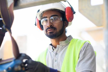 Beyaz miğferi ve güvenlik yeleği olan işçi ahşap bir ev inşa ediyor.