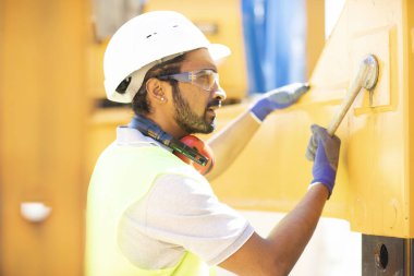 Beyaz miğferi ve güvenlik yeleği olan işçi ahşap bir ev inşa ediyor.