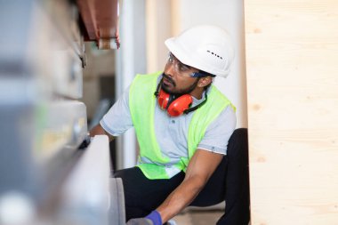 Beyaz miğferi ve güvenlik yeleği olan işçi ahşap bir ev inşa ediyor.