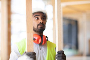 Beyaz miğferi ve güvenlik yeleği olan bir işçi Ahşap bir binada