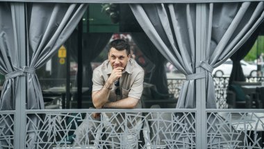 Açık renk gömlekli ve güneş gözlüklü bir adam dekoratif korkuluklara yaslanıyor.