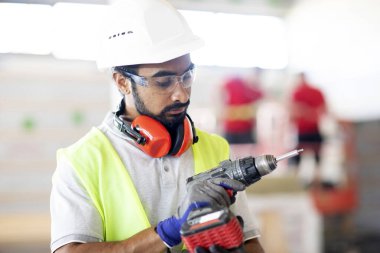 Beyaz miğferi ve güvenlik yeleği olan işçi ahşap bir ev inşa ediyor.