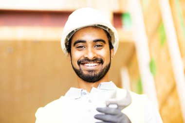 Ahşap bir binada beyaz kasklı ve güvenlik yelekli bir işçi.