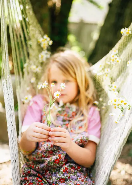 Genç kız elinde çiçeklerle bir hamakta takılıyor.