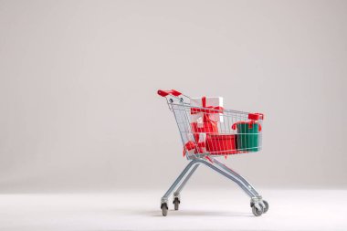 Arka planda paketlenmiş hediye kutularıyla dolu bir alışveriş arabası..