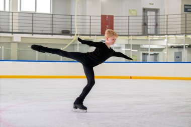 Genç bir erkek artistik patinajcı buz üzerinde bir element üzerinde pratik yapıyor..