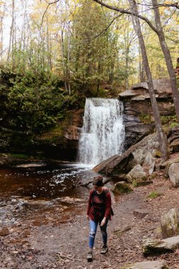 Anne sonbaharda bir şelalenin önünde bebeği taşıyor.