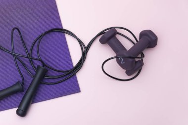 Mor halterler, atlama halatı ve pembe arka planda yoga minderi.