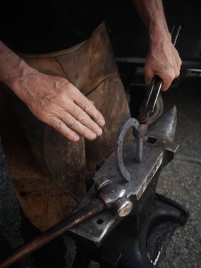Adam çekiçle at nalı yapıyor.