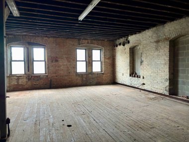 Açıkta tuğla, ahşap zemin ve pencereleri olan boş sanayi dairesi.