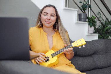 Kadın sarı ukulele çalıyor, evde online müzik dersi.