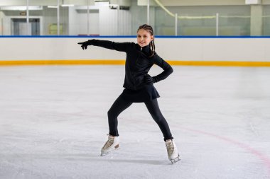 Genç kız artistik patinajcı kapalı bir buz pateni pistinde antrenman yapıyor..