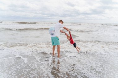 Baba, küçük kızıyla soğuk denizde oynuyor.