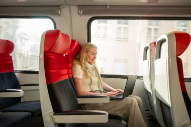 Gündüz vakti trenle seyahat eden bir kadın dizüstü bilgisayarda çalışıyor.