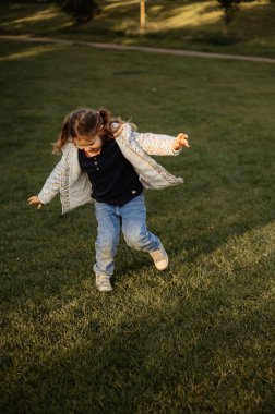 Genç bir kız parkta çimlerin üzerinde oynuyor. Çocukluk mutluluğu.