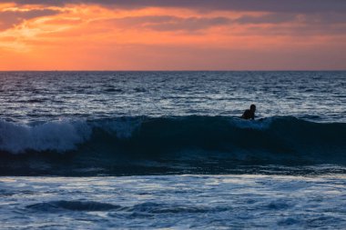 Sörfçü gün batımında limanda doğru dalgayı bekliyor.