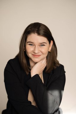 Yüzünde hafif bir ışık olan siyah ceketli, gülümseyen bir kadın.