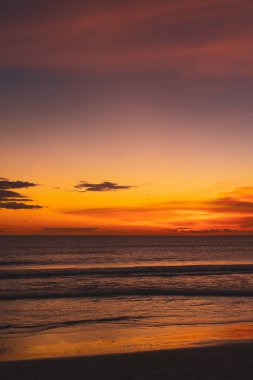 Okyanusun üzerinde turuncu ve mor gün batımı yumuşak dalgalar ve bulutlu gökyüzü