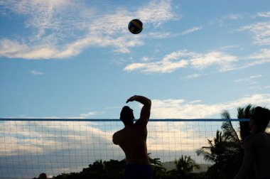 Gün batımında voleybol oynamak için atlayan bir adam.