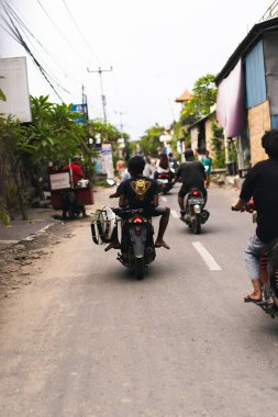 İki Endonezyalı çocuk sörfe gitmek için motosiklete biniyor.