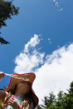Genç kız bulutlu mavi gökyüzüne kabarcıklar üflüyor.