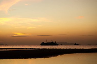 Gün batımında feribot, sakin okyanus ufkuna karşı siluet