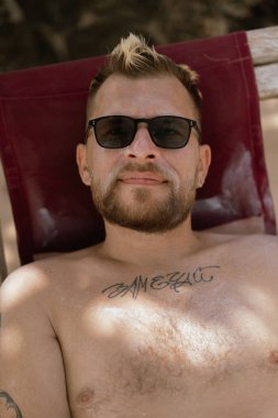 Plajda dinlenen bir adam, benekli güneş ışığı altında.