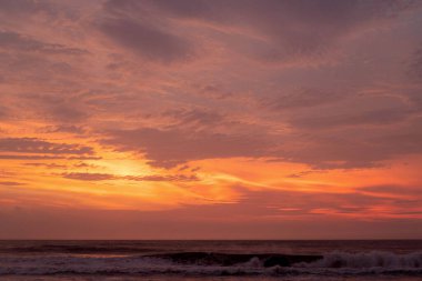 Dalgalar ve dramatik bulutlarla canlı okyanus batımı