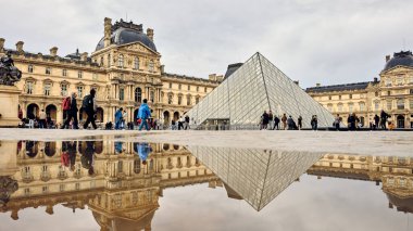 Louvre Müzesi ve piramit Paris 'te yağmurdan sonra su birikintisine yansıyor