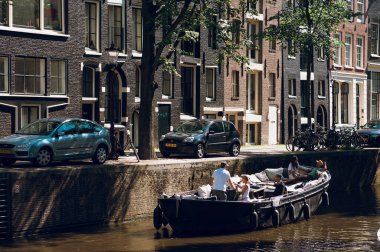 Amsterdam kanalında, tarihi evlerin yakınındaki teknede dinlenen insanlar