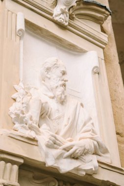 Tarihi taş duvarda kitap tutan sakallı adamın mermer büstü.