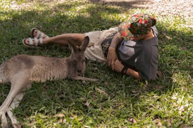 Avustralya vahşi yaşam parkında kangurunun yanında çimlerde dinlenen bir adam.