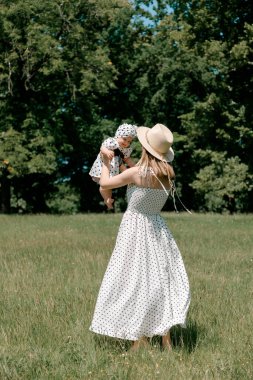 Anne güneşli yaz gününde bebeği çayırda kaldırıyor.