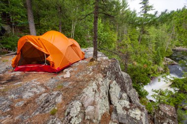 Uçurum kenarındaki bir kamp alanının tepesine turuncu bir çadır kurulmuş.