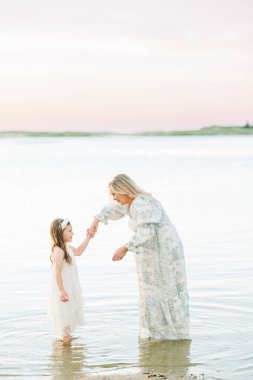 Anne kız el ele tutuşup gün batımında suda oynuyorlar.